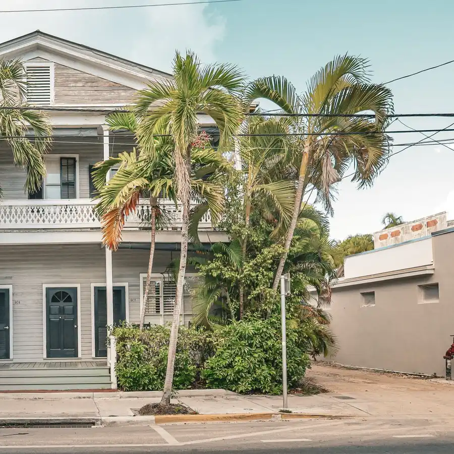 Two-story coastal home with white porches surrounded by palm trees