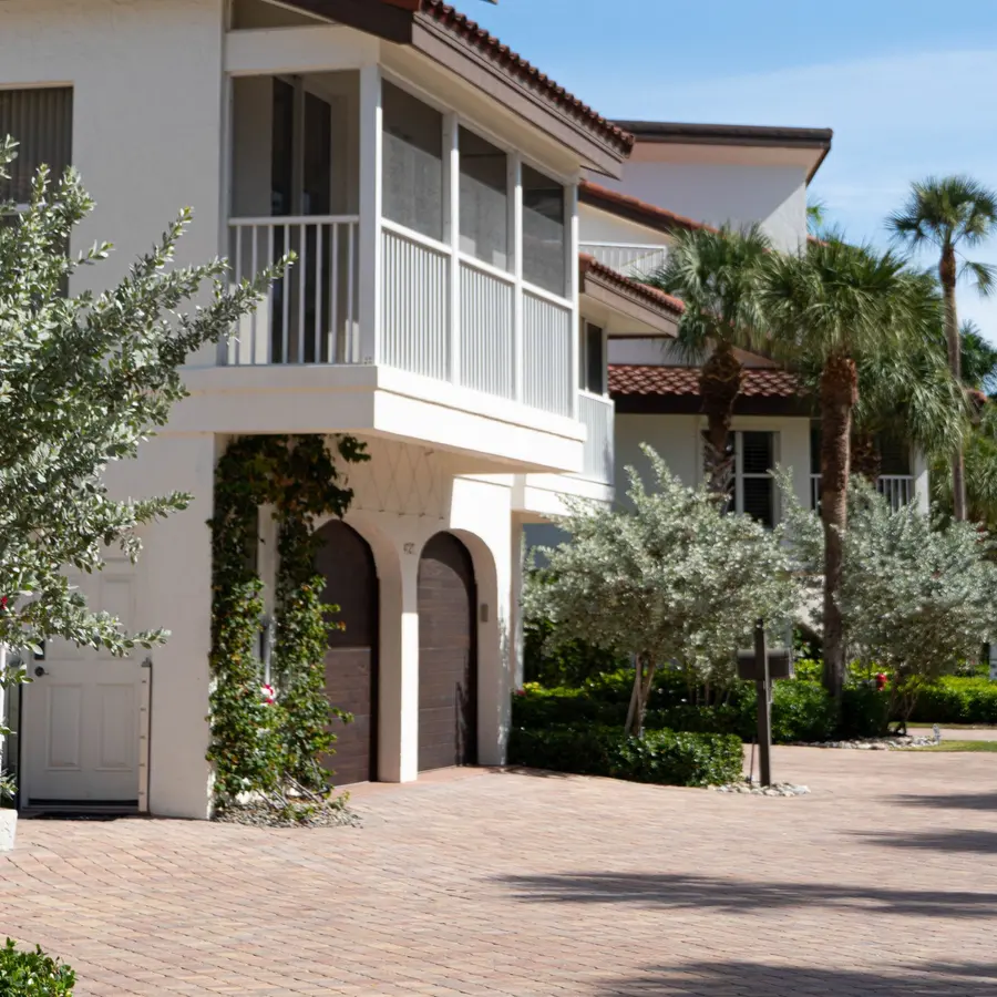 White stucco Florida home with a tile roof, arched garage doors, palm trees and a paver driveway