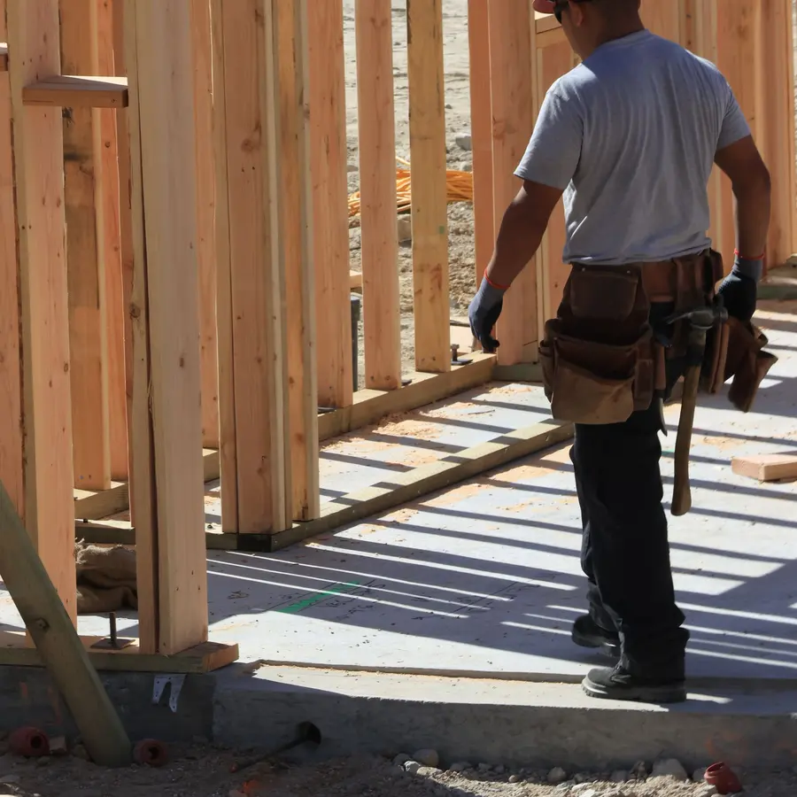 Builder in a hard hat walking through a wood-framed house under construction