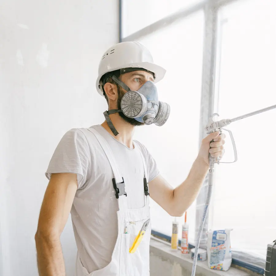 Painter in a hard hat and respirator spraying a wall with an airless spray gun