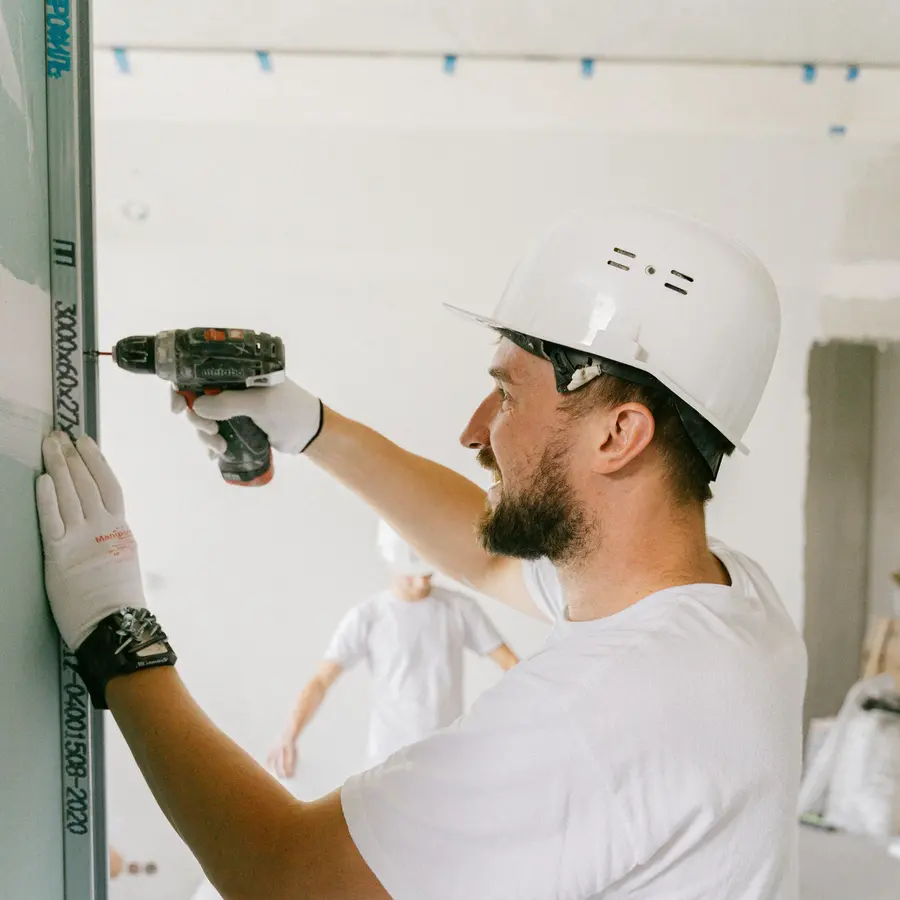 Crew member in a white uniform and hard hat drilling during an interior build-out
