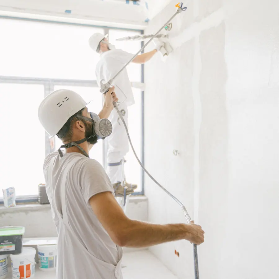 Two painters in white uniforms spray painting a ceiling and walls